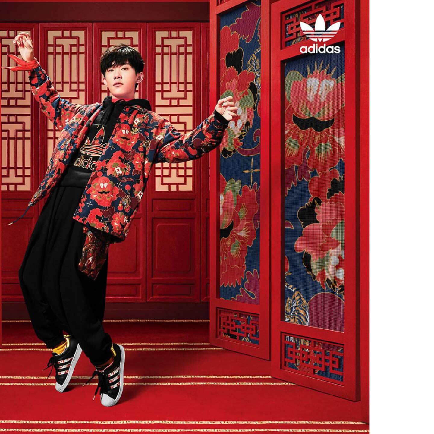 Asian young adult in Adidas patterned jacket poses dynamically against red Asian folding screen and carpet backdrop for Adidas campaign.