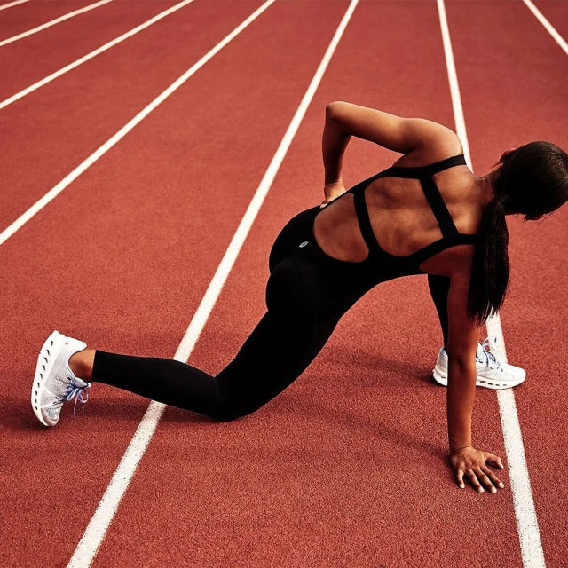 A woman in a black athletic suit stretches on a red running track with white lane markings, showcasing fitness and athletic training.