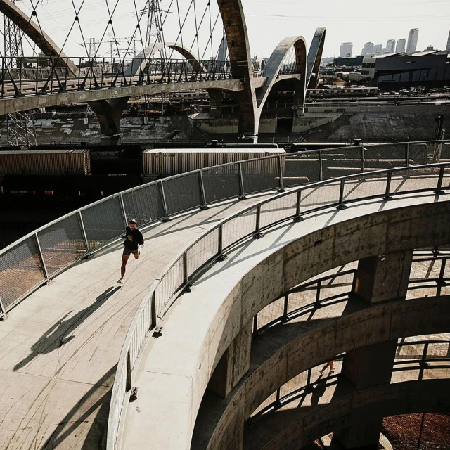 An adult runs on a concrete bridge with rounded architectural elements, while a traditional bridge and cityscape rise in the background.