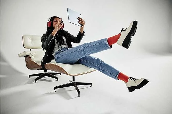 Woman in chair with tablet and headphones. A modern armchair, red socks, and platform shoes add a fashionable touch to this studio shot.