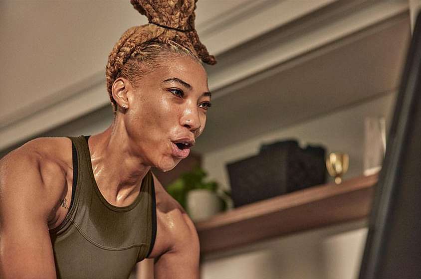 Determined woman with braided hair works out indoors wearing fitness apparel, demonstrating strength, sweat, and healthy lifestyle choices.