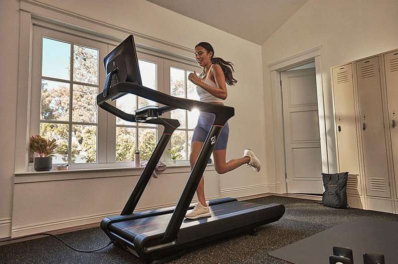 A woman exercises on a treadmill indoors at home with a view of the outside through a window, promoting a healthy and active lifestyle.