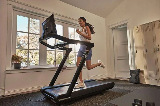 A woman exercises on a treadmill indoors at home with a view of the outside through a window, promoting a healthy and active lifestyle.
