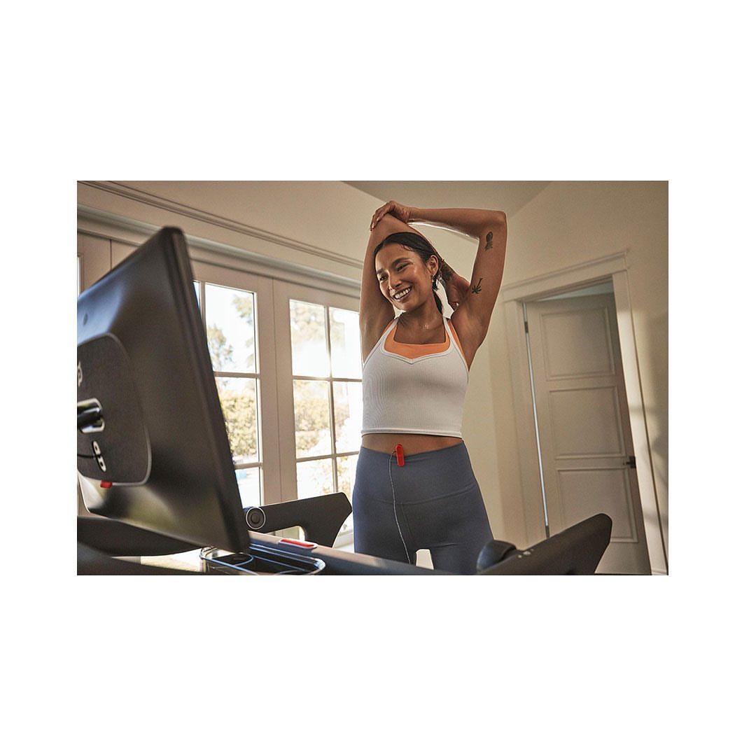 Woman stretches on an exercise bike inside a bright home. Fitness equipment in an indoor setting. Healthy lifestyle concept with natural light.