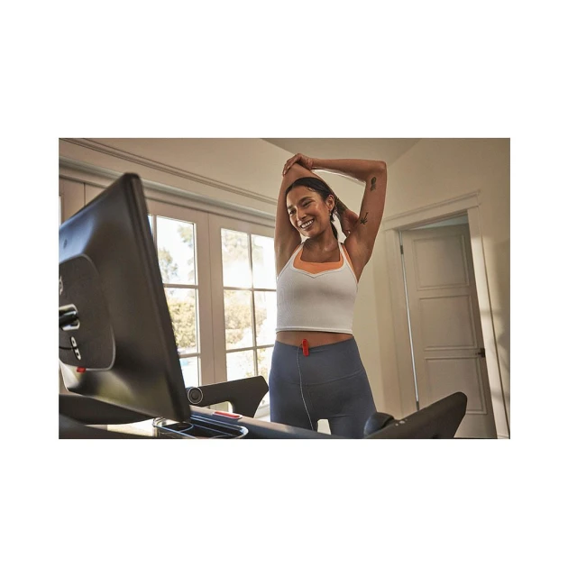 Woman stretches on an exercise bike inside a bright home. Fitness equipment in an indoor setting. Healthy lifestyle concept with natural light.