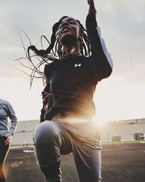 Athletic woman in sportswear leaps on a track during a workout on a sunny day. Fitness and healthy lifestyle in outdoor setting.