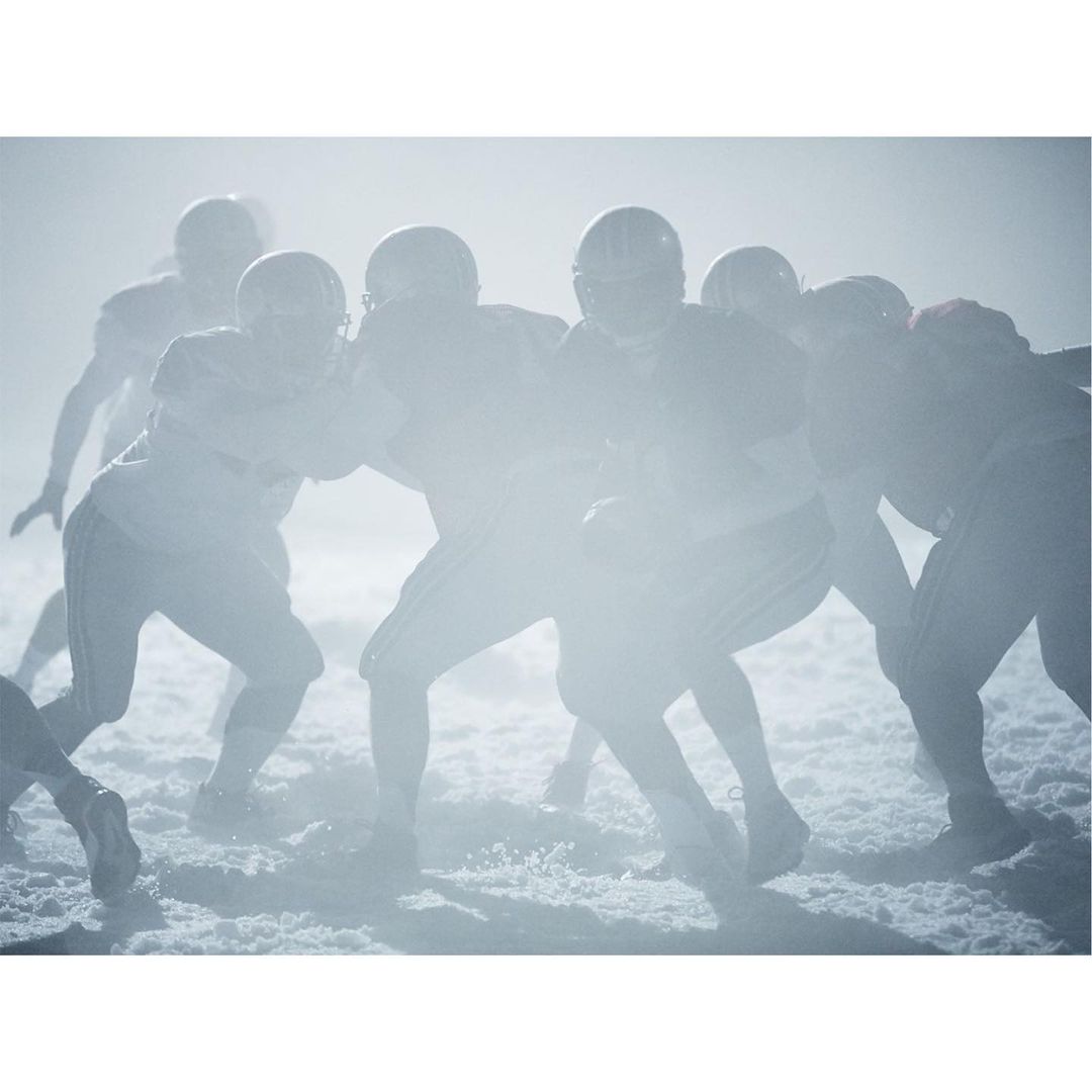 American football players in uniform during game with helmets on, in a foggy outdoor setting, showcasing action and team sport.