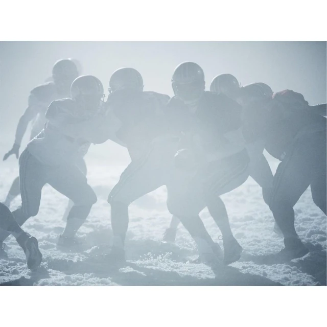 American football players in uniform during game with helmets on, in a foggy outdoor setting, showcasing action and team sport. 