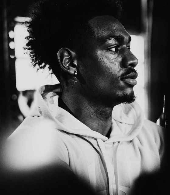 Black and white portrait of a handsome Black man with an earring and a hoodie looking off to the side in a softly lit indoor area.