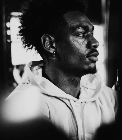 Black and white portrait of a handsome Black man with an earring and a hoodie looking off to the side in a softly lit indoor area.