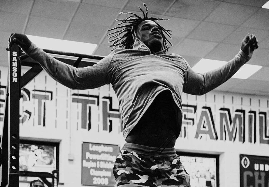 A muscular African-American athlete performs a pull-up in a workout setting, showcasing strength and fitness in a monochrome aesthetic.