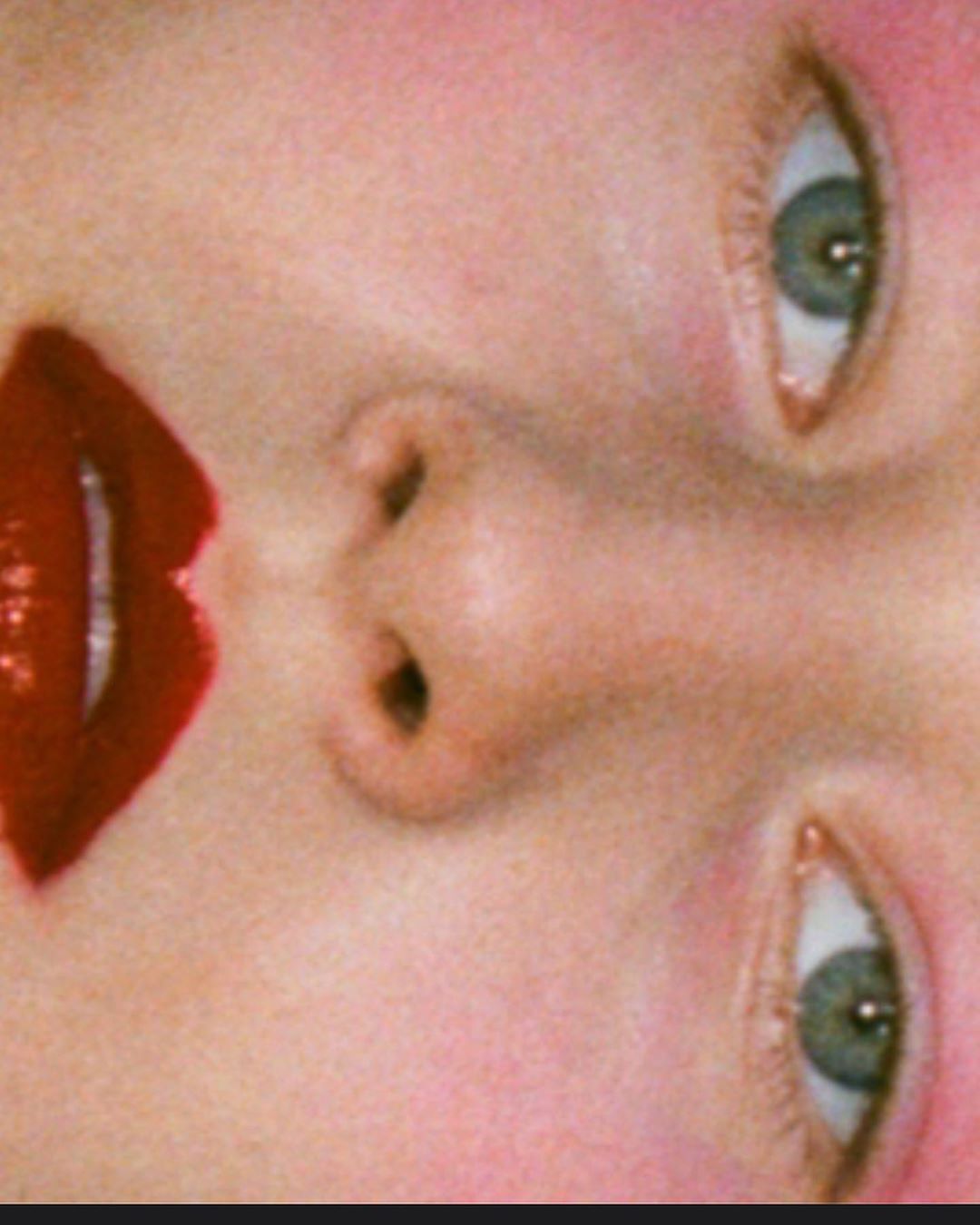 Close-up of a person's face with bright red lipstick, visible eyes, and nose, rotated to the side, showcasing detailed skin texture.