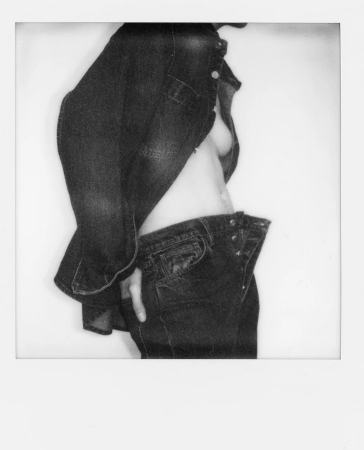 Monochrome image of an unbuttoned denim jacket and jeans on a person, set against a stark white backdrop, creating a studio-style portrait.