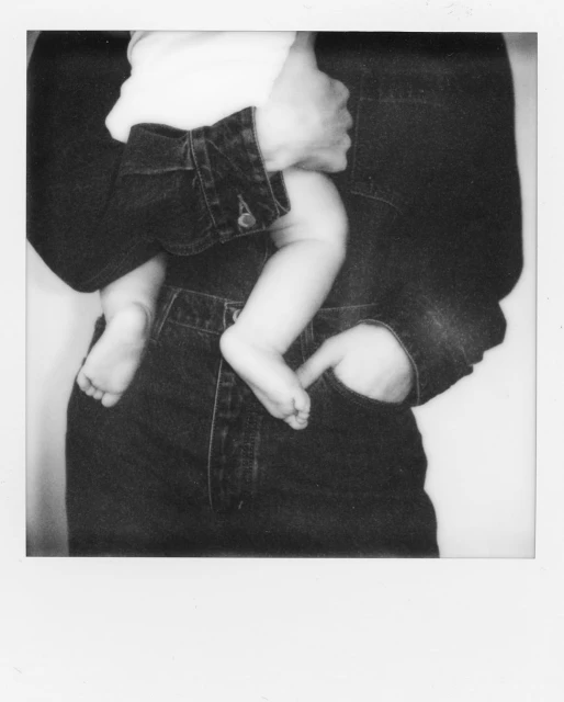 Monochrome photo of an adult holding a baby, emphasizing the denim jacket and jeans, capturing a moment of parental affection and care.