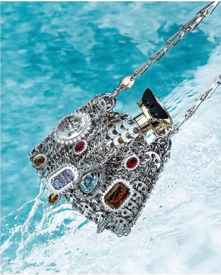 Ornate silver metal handbag with gem embellishments displayed partially submerged in clear blue water, fashion and luxury concept.