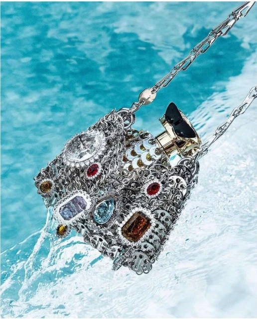Ornate silver metal handbag with gem embellishments displayed partially submerged in clear blue water, fashion and luxury concept.