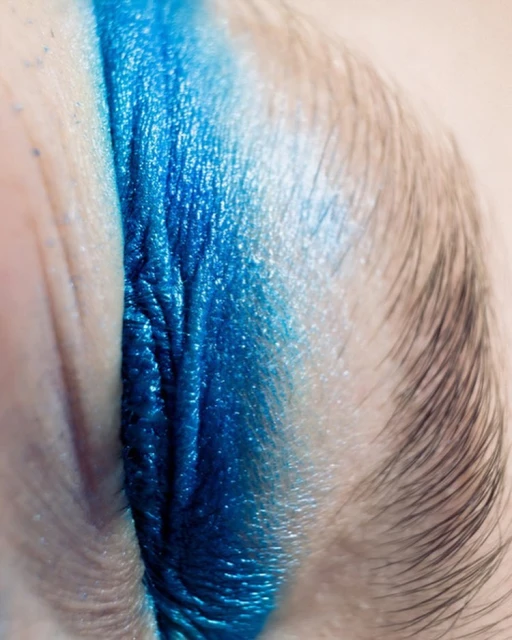 Close-up of a closed eye with a vibrant, shimmering, blue eye shadow creating a bold and striking visual effect in beauty shot.