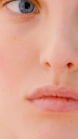 Close-up of fair-skinned young adult female face with blue eyes, lips, and nose in a beauty or fashion context.