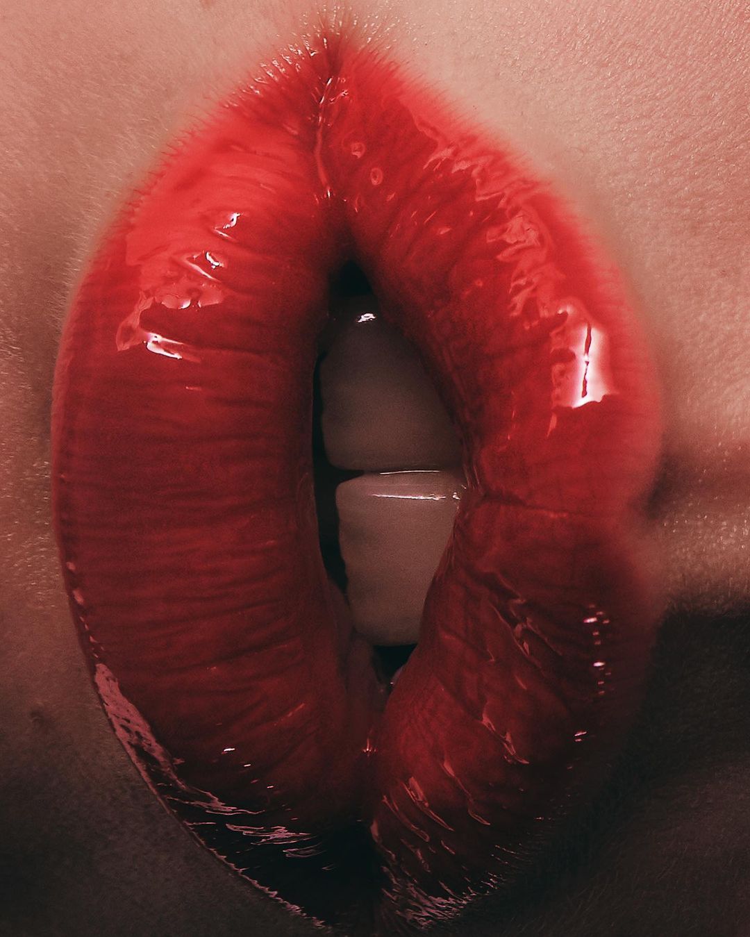 Close-up shot of a person's mouth with bright red lipstick, showcasing teeth slightly parted. The lips are glossy and prominent.