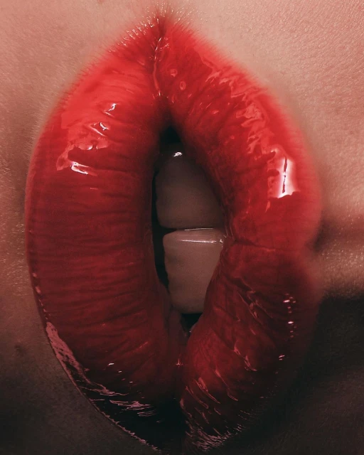 Close-up shot of a person's mouth with bright red lipstick, showcasing teeth slightly parted. The lips are glossy and prominent.