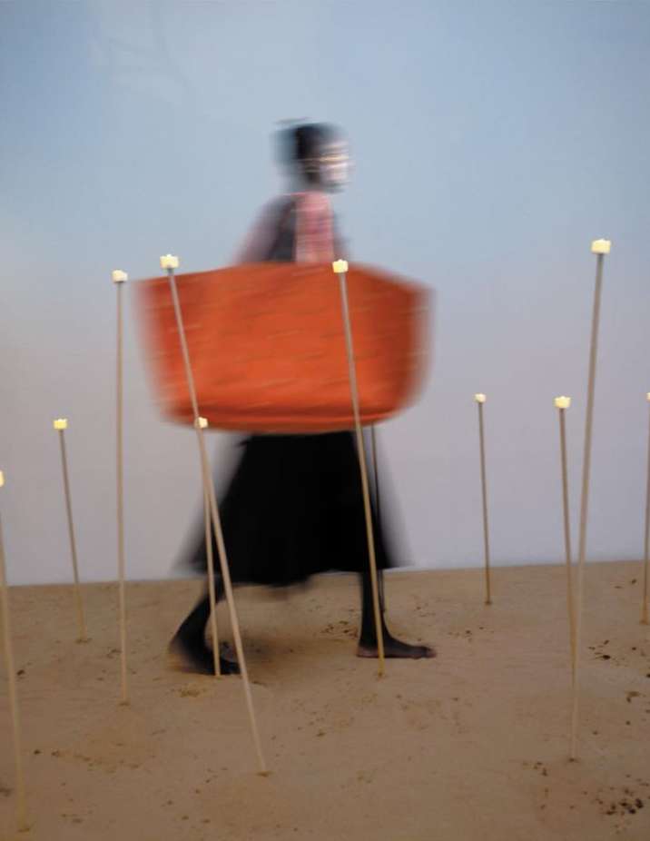 Abstract blurred shot of a person carrying a basket walking on a sandy surface with multiple sticks with glowing tips. 