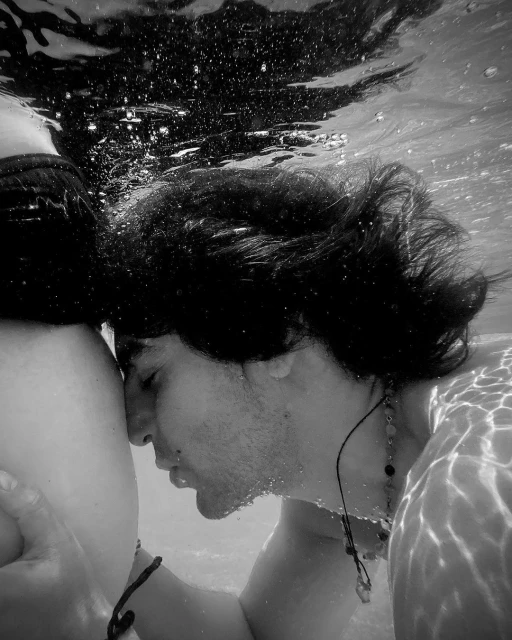 Black and white underwater shot featuring a close-up of two people with dark hair, one leaning against the other in the water.