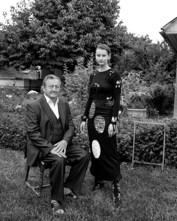 Black and white portrait of a man seated on a chair next to a standing woman in an outdoor garden setting in London.