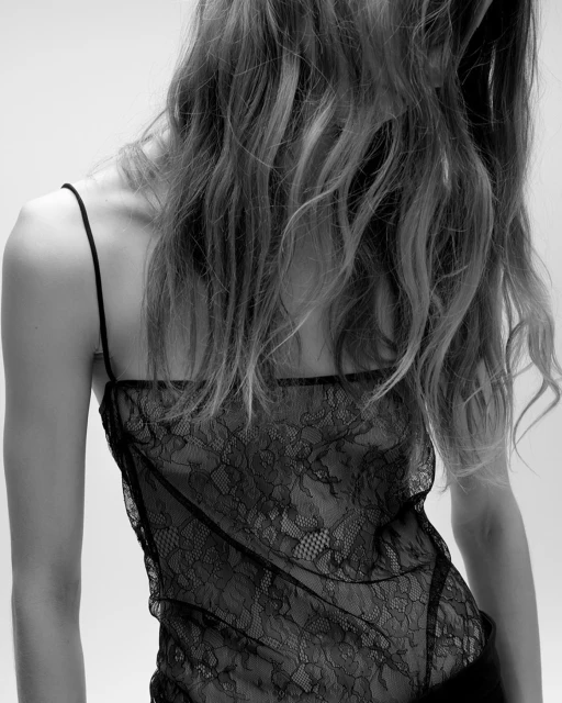 Back view of a slender adult female with flowing wavy hair, wearing a black lace top in a studio setting with a white background.