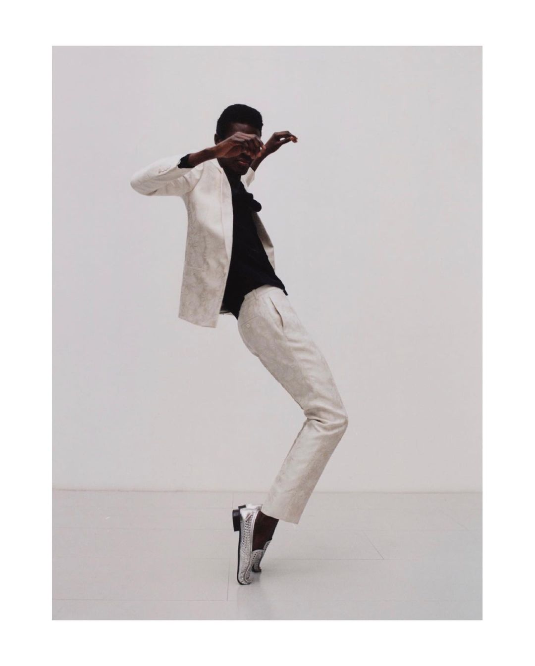 Man in off-white suit strikes dynamic pose against a white backdrop, showcasing high fashion and expressive movement.
