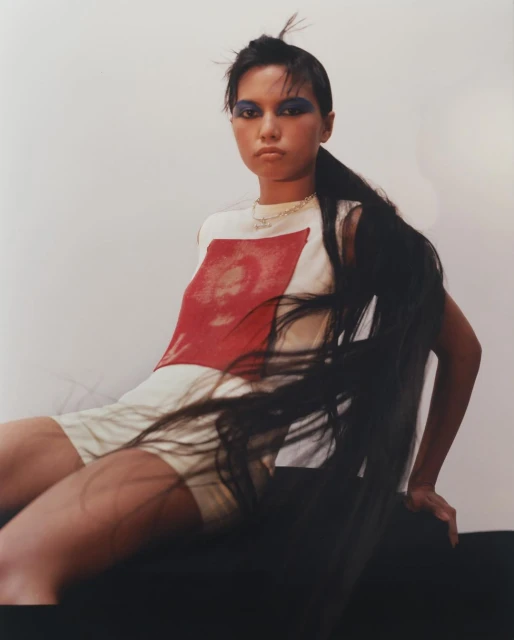 Portrait of a young woman with long hair extension, wearing a graphic tee and shorts, posing in a photo studio setting. Fashion photography.