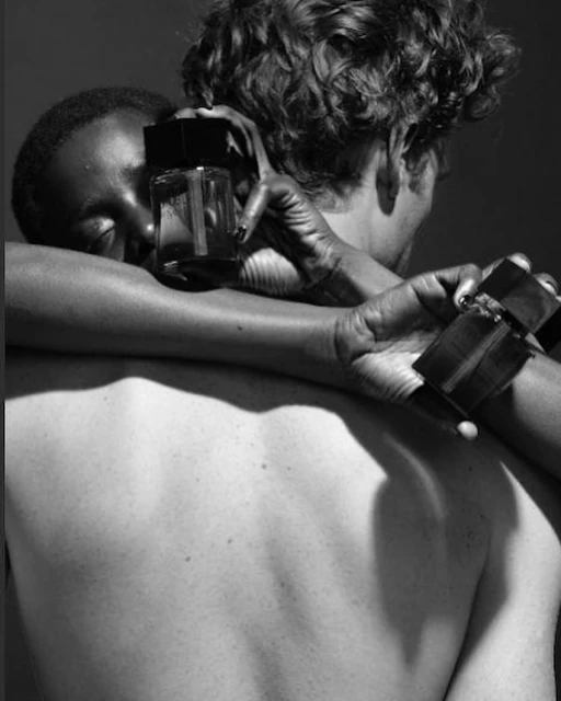 Black and white studio shot featuring two models holding perfume bottles, with one model resting their head on the other's back.