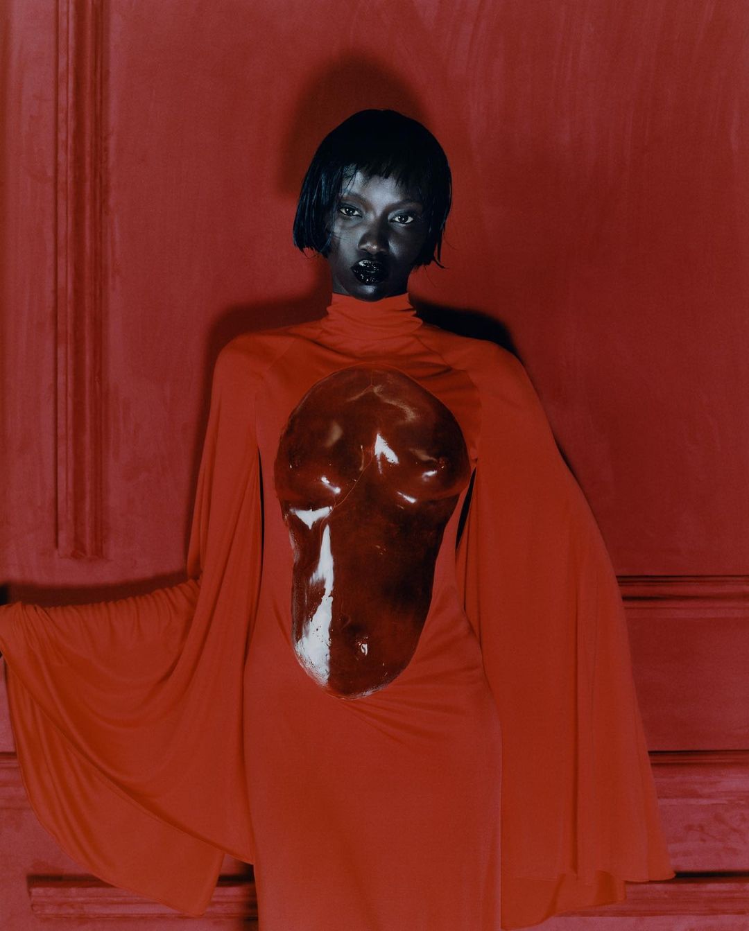 Elegant fashion portrait of a black model wearing a red dress with abstract bodice art against a matching red backdrop.