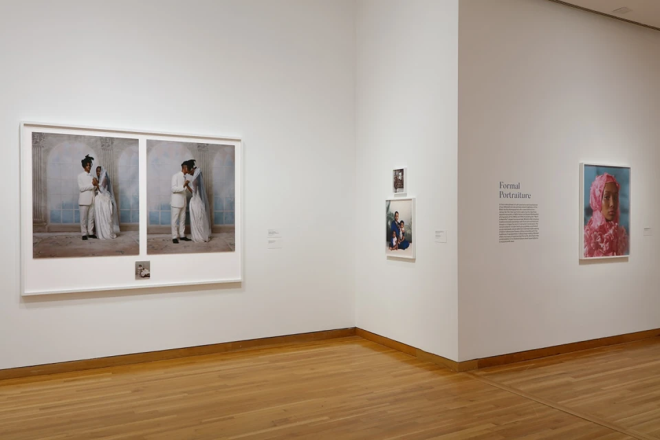 Two framed wedding photos of a bride and groom on display in an art gallery with multiple other images and a light wood floor.