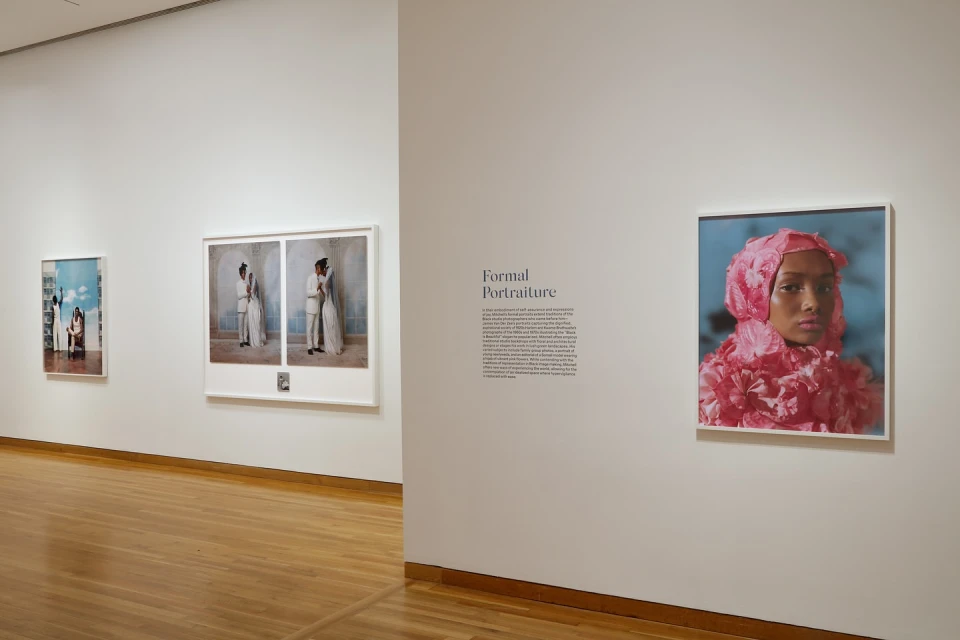 Interior museum view of three framed portraits on a white wall with a light brown wood floor in the foreground of the scene.