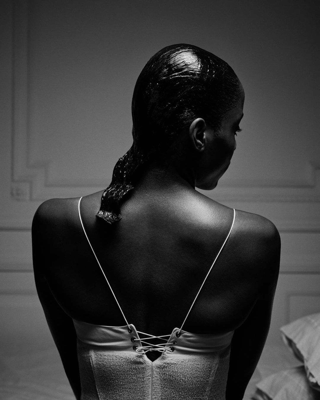 Monochrome portrait of a Black woman from behind, wearing a strappy white top with back lacing and wet hair, by Tyler Mitchell.