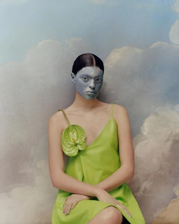 Woman with grey face paint wearing a green dress poses in front of a painted blue and white cloud background in a studio shot.