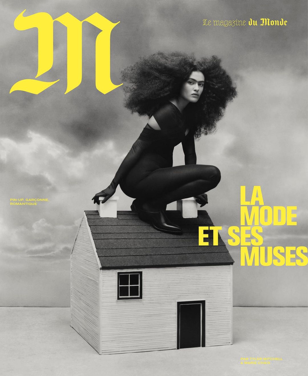 Magazine cover featuring a woman with afro-style hair kneeling on a miniature house, against a cloudy sky. Fashion and editorial.