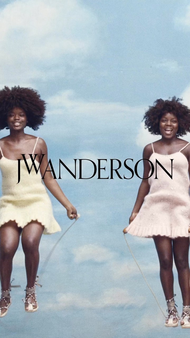 Two African-descent women jump rope in pastel dresses and gladiator sandals against a bright sky with wispy clouds, fashion editorial.