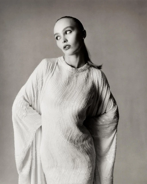 Monochrome portrait of a woman wearing a white, textured dress with long sleeves, posing against a neutral backdrop in a studio setting.
