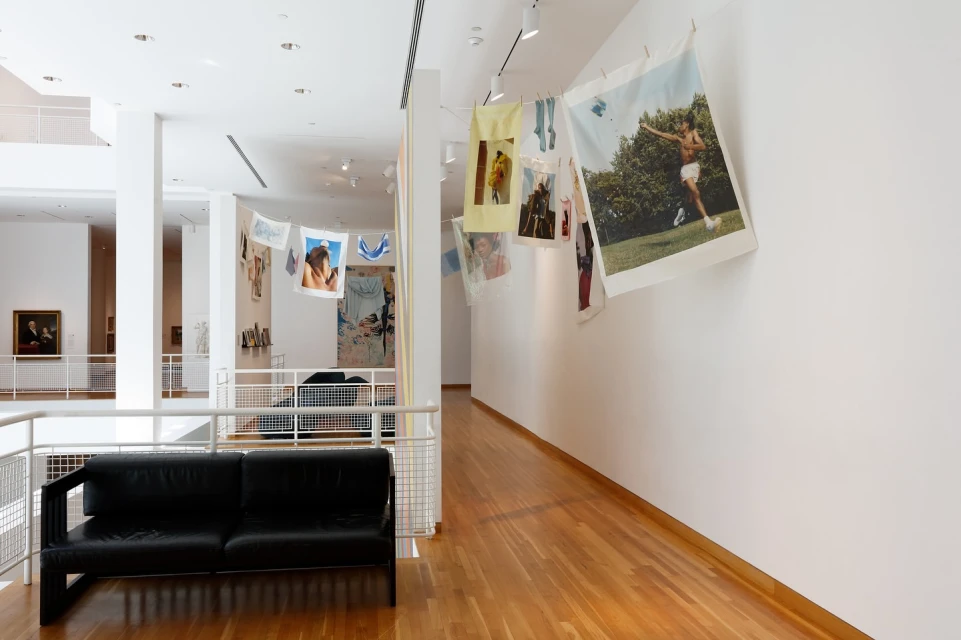 Museum installation displays photographs hanging on a line inside a brightly lit, modern art gallery with white walls and wood floors.