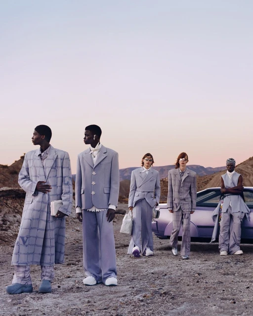 Five fashion models in light purple suits pose outdoors on a desert landscape near a matching purple car in a fashion editorial shoot.