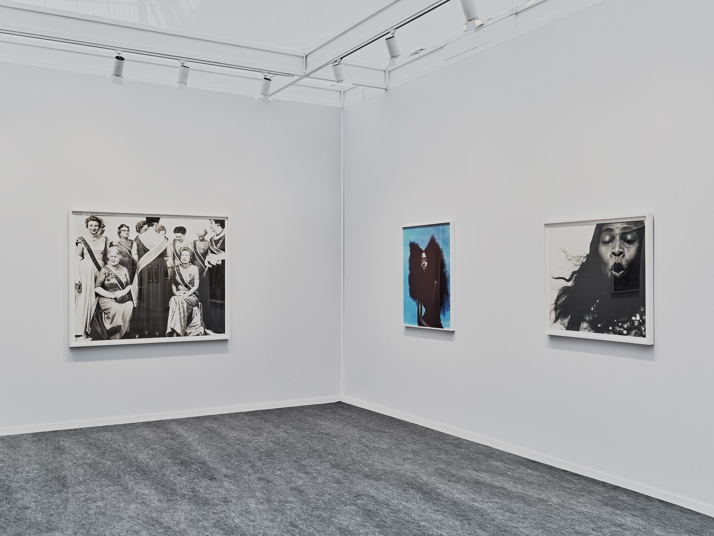 Interior view of a bright art gallery with three framed artworks on a white wall, including a group portrait and two modern art pieces.