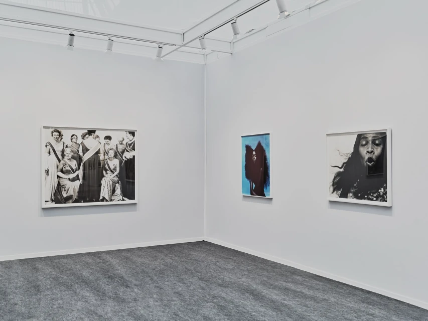 Interior view of a bright art gallery with three framed artworks on a white wall, including a group portrait and two modern art pieces.