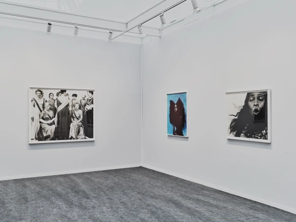 Interior view of a bright art gallery with three framed artworks on a white wall, including a group portrait and two modern art pieces.