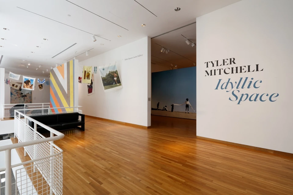 Art gallery interior featuring 'Tyler Mitchell: Idyllic Space' exhibit, with photographs and prints displayed against white walls and wood flooring.