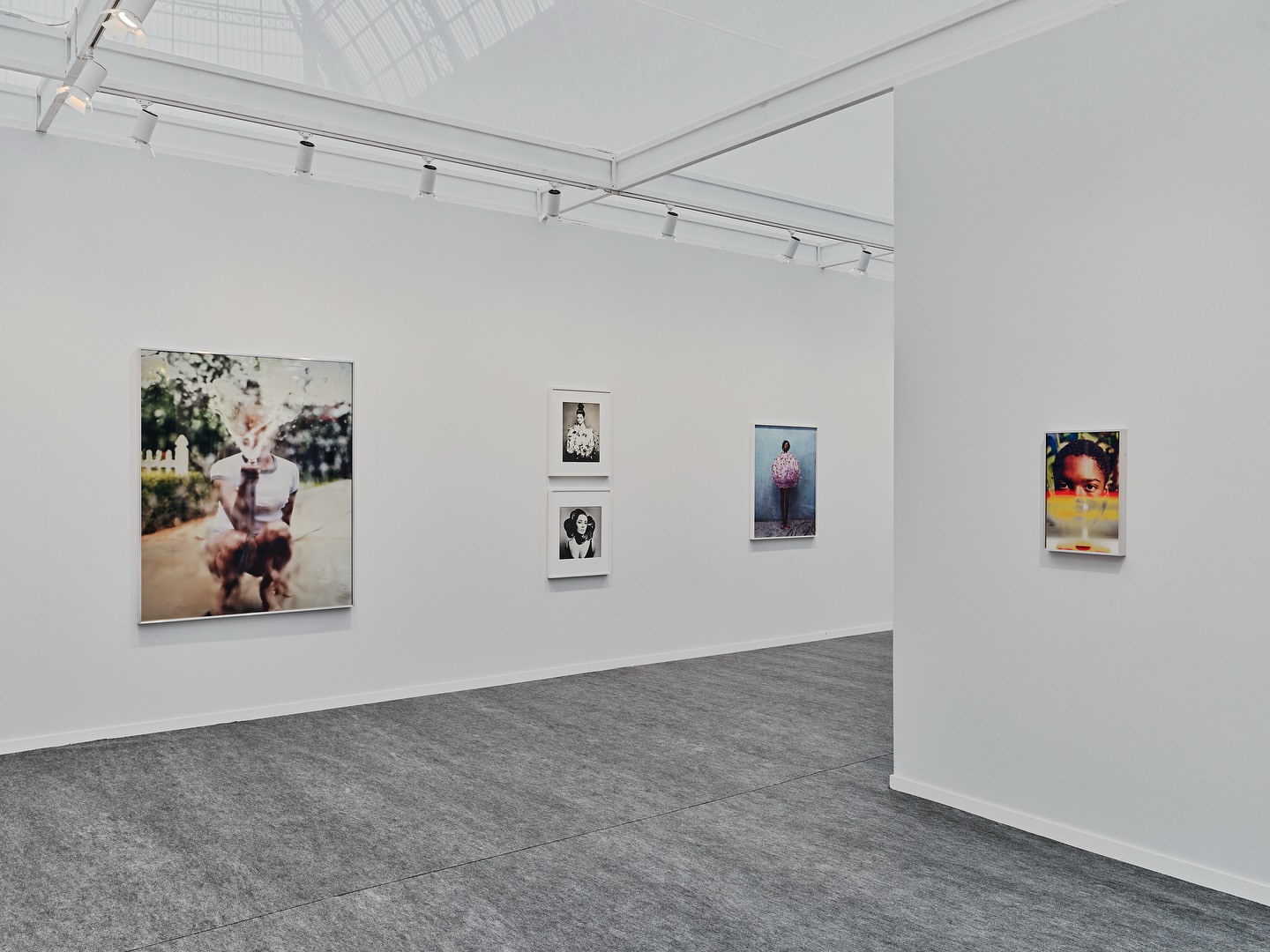 An art gallery featuring photographic portraits and minimalist architecture with white walls and gray floors illuminated by track lighting.