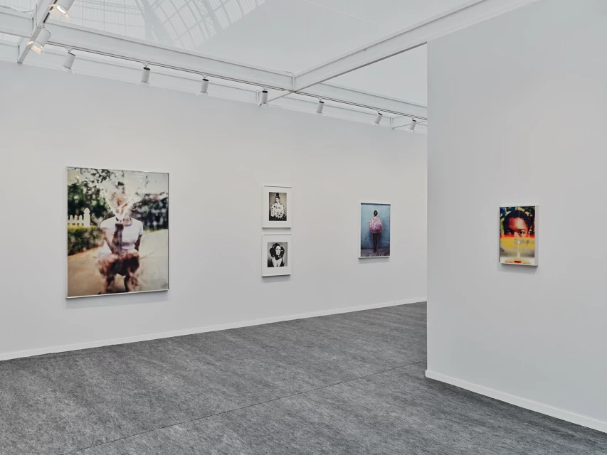 An art gallery featuring photographic portraits and minimalist architecture with white walls and gray floors illuminated by track lighting.