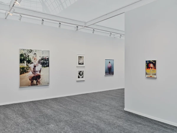 An art gallery featuring photographic portraits and minimalist architecture with white walls and gray floors illuminated by track lighting.