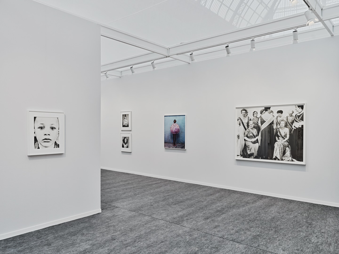 Interior view of an art gallery with multiple framed photographs hanging on the walls and gray flooring, illuminated by track lighting.