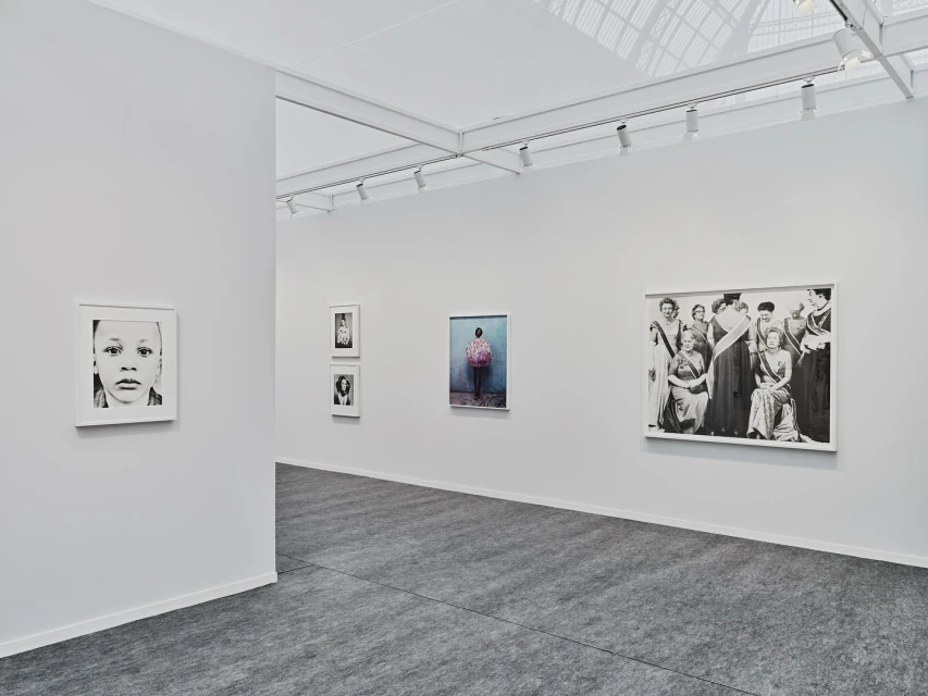 Interior view of an art gallery with multiple framed photographs hanging on the walls and gray flooring, illuminated by track lighting.